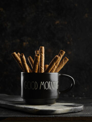 Fragrant cinnamon sticks in a black cup on a black background. Spices, aromatic additives to drinks. Ingredient for confectionery. Minimalism. There are no people in the photo.