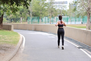 Portrait of sporty young asian woman in sportswear jogging outdoor for marathon training. Jogger girl exercising along concrete path outdoor with green tree background. Sport concept