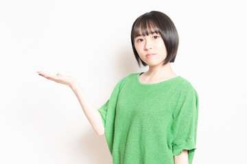 白背景の前で案内のポーズをする若い女性