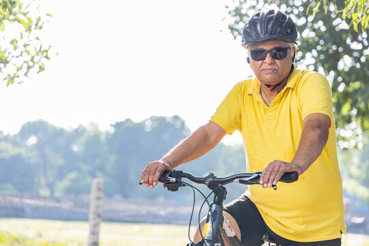 Thoughtful senior man in protective sportswear leaning on bicycle handlebar outdoors
