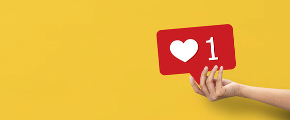 Hand holding shape of red speech bubble with heart on yellow background.Hand holding shape of red speech bubble with heart on yellow background.