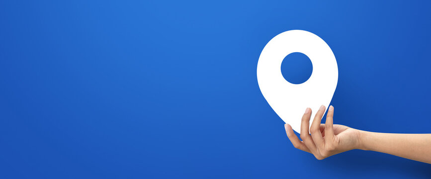 Hand holding shape of white location icon on blue background.