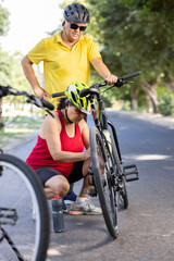 Fototapeta na wymiar Senior couple repairing broken bicycle on road during morning ride 