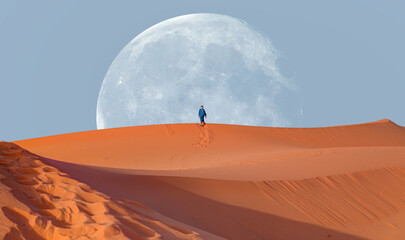 Happy bedouin in traditional bright clothing standing on sand in sahara desert with super full moon - Sahara, Morocco 