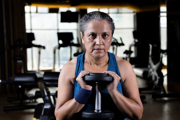 Old woman in sportswear exercising with dumbbell at gym

