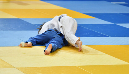 Fighter girls judoists in kimonos compete on the tatami 
