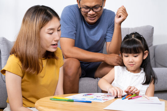 Young Asian girl feeling fun and happy while drawing color paint with her mother and father inside of the living room. Family relationship and learning art activity, togetherness and bonding.