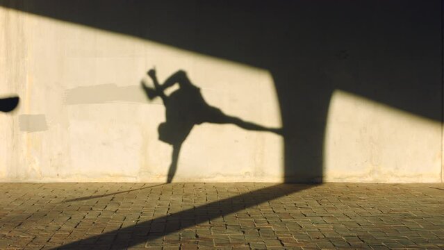 Dance, shadow and hip hop dancer to music while training for performance outdoor. Freedom, art and creative young guy dancer moving to the rhythm or beat of a song with a gray background