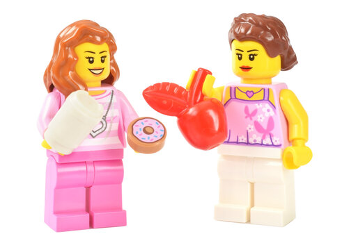 Lego minifigure happy cute girl with donut and coffee to go cup and women with red apple fruit.  Editorial illustrative image of model healthy and unhealthy  food.