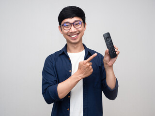 Asian positive man wear glasses smile point finger at remote in his hand isolated