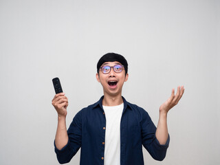 Cheerful asian man holding remote tv feels amazed looking above isolated
