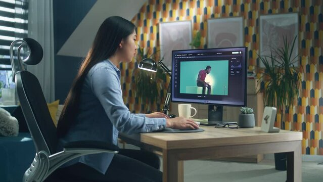 Asian woman editing photo in photoshop for customer on personal computer while sitting at the table at home office and working remotely