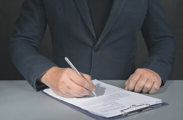 Businessman signs contract. Holding pen in hand. Businessman signing contract at table. Signing legal document. dark background
