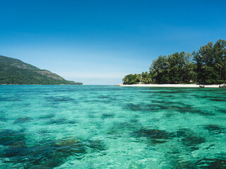 Scenic view of Sunset Beach, Koh Lipe Island. White sand beach tropical island, crystal clear turquoise sea with coral reef transparent water against summer blue sky. Satun, Thailand.