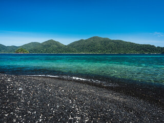 Scenic view of Koh Hin Ngam Island iconic black pebble stone beach against crystal clear turquoise sea and summer blue sky. Near Koh Lipe Island, Tarutao National Marine Park, Satun, Thailand.
