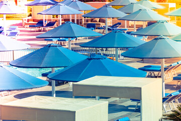 Lots of beach umbrellas on an empty evening beach. Evening beach on the sea in cloudless weather. Sunset on a sandy beach with sun umbrellas and sun loungers
