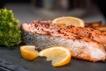 Fryed salmon fillets background on a black plate with lemon slice, french fries and boiled broccoli. Grilled salmon fillets on a grill plate sprinkled with spices