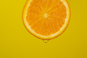 Water falling from orange hue orange on yellow background. Orange slice and water splashing, drops of juice falling from juicy fruit. Making cocktail of fruits, drinking cold lemonade © Oleg