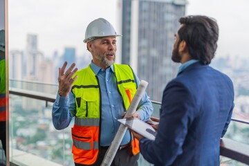 Fototapeta na wymiar Portrait photo of a white caucasian construction architect holding a architecture plan discussing the project details with his client an asian businessman holding a digital tablet