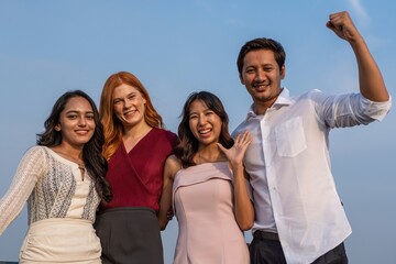 Photo of a group of friends cheering and posing for a group photo together in a rooftop bar in the city of Bangkok while touring the site as tourists during a sunset time