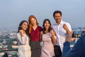 Photo of a group of friends cheering and posing for a group photo together in a rooftop bar in the city of Bangkok while touring the site as tourists during a sunset time