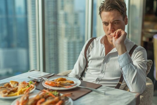 Photo of a handsome caucasian white male guy model look confused and thoughtful or feeling lost during a luxurious lunch as he just had a quarrel with his girlfriend
