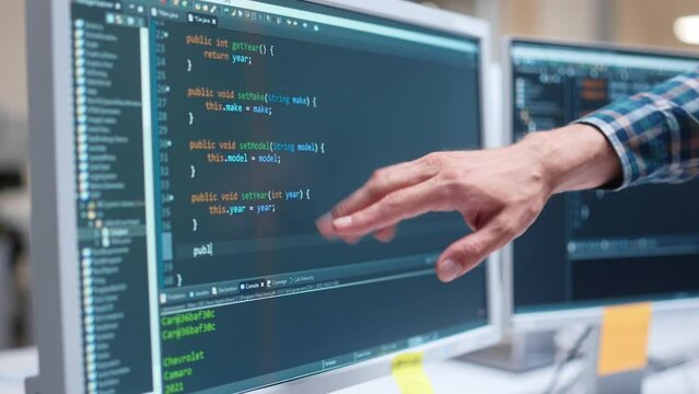 Close up computer screen with html code language. IT programer working on desktop computers typing on computer coding a program. Hand pointing at monitor with sophisticated programming code