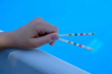 Pool test strips in the child's hand. Blue pool background. Water balance.