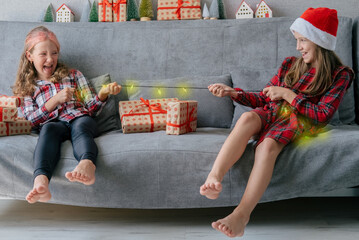 Two happy sisters are pulling the garland like a rope. Children play on New Year's Eve at home.