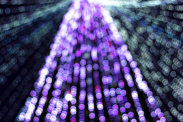 Festive purple xmas lights on christmas tree in urban central park at holiday winter night, defocus shiny garland decoration glow in lilac bokeh in dark downtown, out of focus image