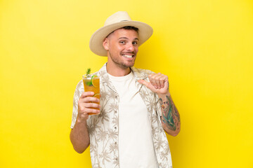 Young caucasian man holding a cocktail isolated on yellow background proud and self-satisfied