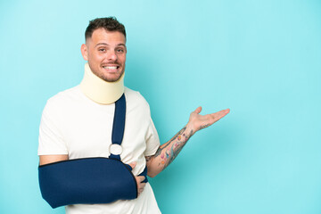 Young caucasian man wearing a sling  and neck lace isolated on blue background extending hands to...