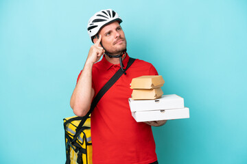 Young caucasian man with thermal backpack and holding fast food isolated on blue background having doubts and thinking