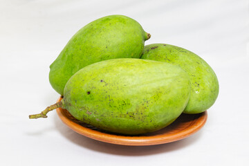 unpeeled green mangoes on clay plate. studio photo shoot.