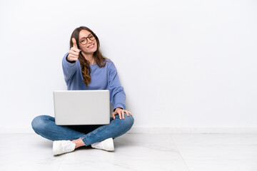Young caucasian woman with a laptop sitting on the floor isolated on white background with thumbs...