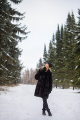 Fototapeta na wymiar irl in a black hat and a fur coat stands on a snowy winter alley