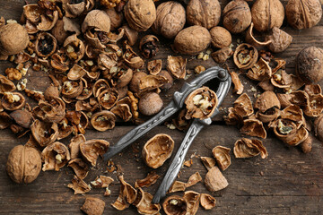 Walnuts, pieces of shells and nutcracker on wooden table, flat lay