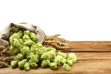 Overturned sack of hop flowers and wheat ears on wooden table against white background, space for text