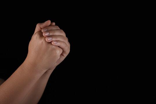 Woman holding hands clasped while praying on black background, closeup. Space for text