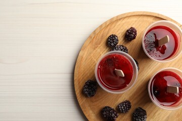 Tasty berry ice pops in plastic cups and space for text on white wooden table, top view. Fruit popsicle