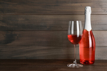 Bottle and glass of delicious rose wine on table against wooden background. Space for text