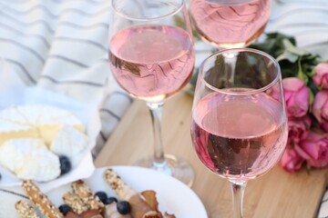 Glasses of delicious rose wine, flowers and food on white picnic blanket, closeup
