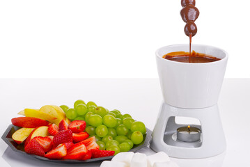 Chocolate fondue. fruits dipping into bowl with chocolate on white background. Close up of warm,...