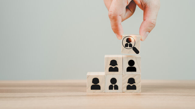 Hand hold wood cubes with magnifying glass focuses on the best employee icon to be a team leader for recruitment managers, and target customer concepts. HRM or Human Resource Management.