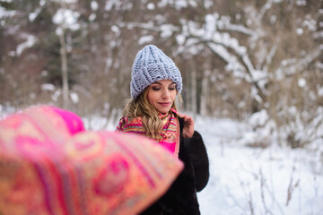 girl in a blue hat, black fur coat and fluttering pink flying scarf among the snowy forest