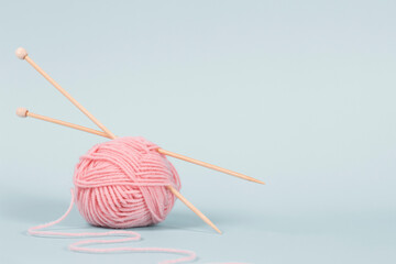 One thread ball and wooden bamboo knitting needles on light blue background. Hobby, relaxation, mental health, sustainable lifestyle