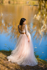 girl in a beautiful light puffy dress on the shore of a pond with blue water