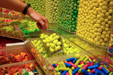 candy store. Woman hand with scoop taking colorful delicious candies on counter of shop, grocery, market, cafe. Many colorful candies on grocery stand Dessert, sale, sweet food and confectionery