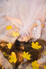 girl in  wedding fluffy chiffon dress on clear day lies among the fallen autumn maple leaves