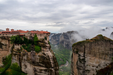 Scenic view of Holy Monastery of Varlaam on cloudy foggy day, Kalambaka, Meteora, Thessaly, Greece, Europe. Rock formations overgrown with green moss creating moody atmosphere. UNESCO World Heritage